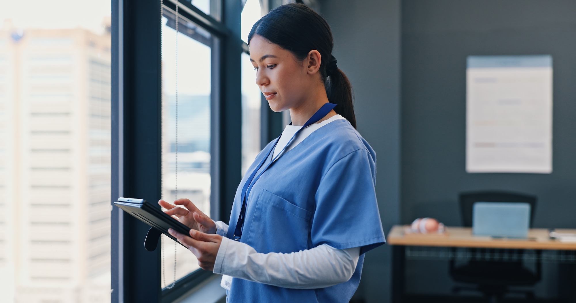 A registered nurse reviewing digital patient records on a tablet in a modern clinical facility.