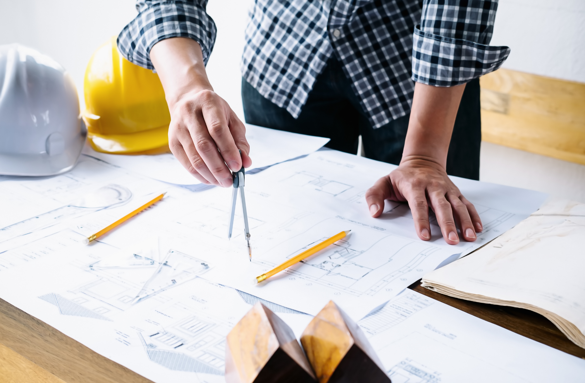 A project manager planning architectural blueprints on site with drafting tools and safety hard hats nearby