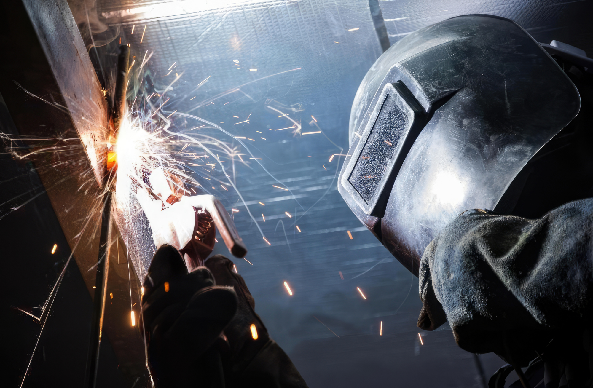 A skilled trade welder wearing protective gear while fabricating heavy structural steel components